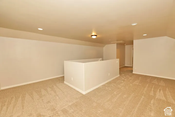 Neutral-toned interior space featuring neutral carpeting, recessed lighting, slanted ceilings, and a central partition wall