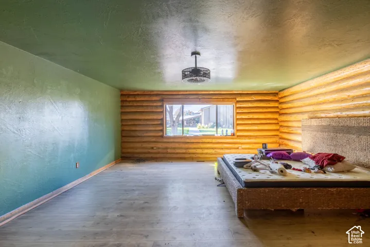 Interior room featuring horizontal log walls, wood-finish flooring, a painted accent wall, and a centrally mounted caged ceiling fan
