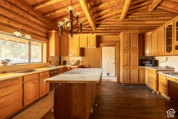 Rustic kitchen featuring exposed log walls, vaulted wood-beam ceiling, wood cabinetry, a central island with a countertop, and a multi-light chandelier