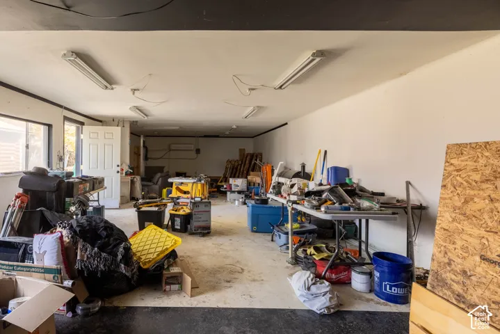 Multi-bay garage featuring expansive floor space, multiple linear overhead light fixtures, wall-mounted heating and cooling unit, and dual-entry access