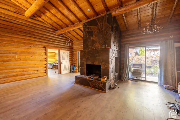 Log-walled interior featuring an exposed timber beam ceiling, stone-faced hearth and fireplace, wood-finish flooring, and antler-style chandeliers