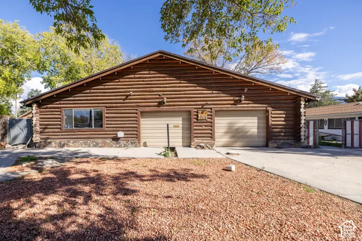 Log-style exterior featuring stacked stone foundation, dual garage bays, and concrete driveway