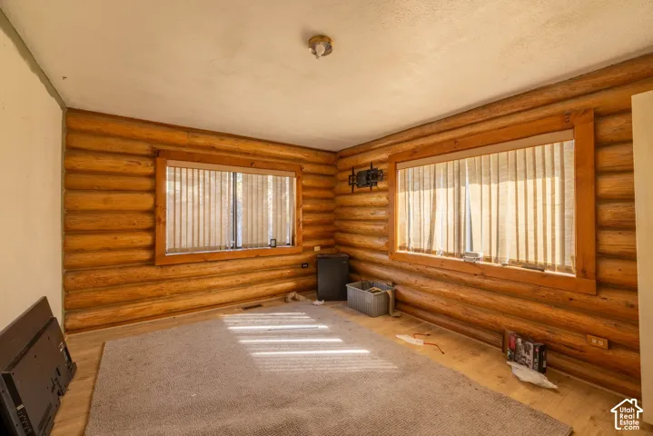Interior space featuring exposed log walls, two windows with wood-trim framing, and light-toned flooring