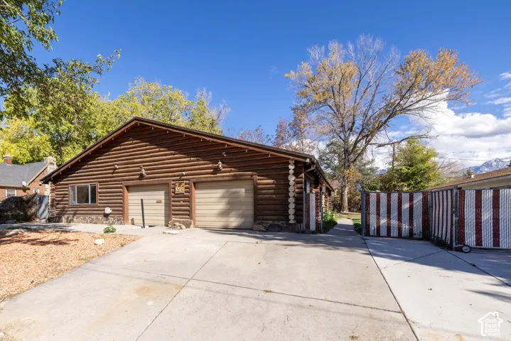 Log exterior structure featuring a two-car garage, concrete driveway, stone foundation accents, and gated side access