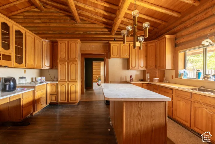 Kitchen featuring vaulted timber ceiling, exposed log walls, stained wood cabinetry, central island with stone-finish countertop, and metal chandelier