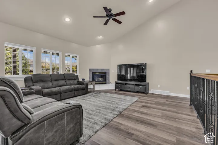 Vaulted ceilings, wood-finish flooring, corner fireplace with tile surround, ceiling fan, and ornate metal railing