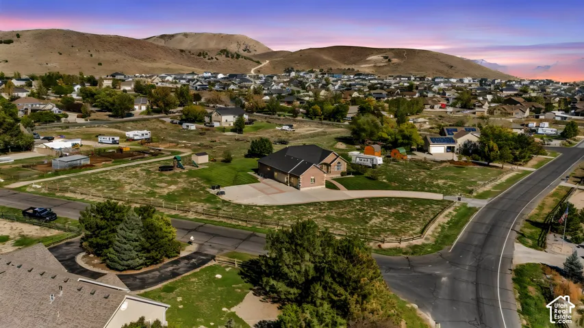 Aerial perspective featuring a single-story brick exterior, expansive lot, asphalt-shingled roof, concrete driveway, and mountain backdrop