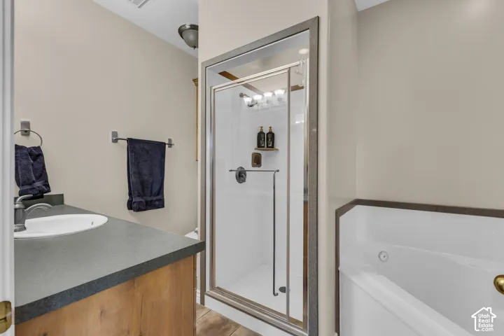Bathroom featuring a wood-finish vanity with a matte countertop, drop-in sink, glass-enclosed shower with metallic framing, and a deep soaking tub