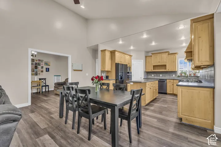 Vaulted ceiling, wood-finish flooring, shaker-style natural wood cabinetry, central kitchen island, and recessed lighting