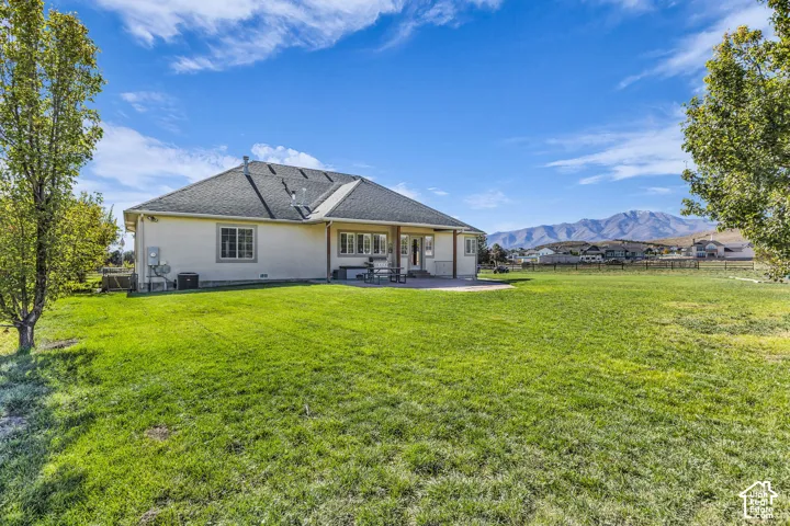 Expansive backyard featuring a sprawling lawn, paved patio, mature trees, and mountain backdrop