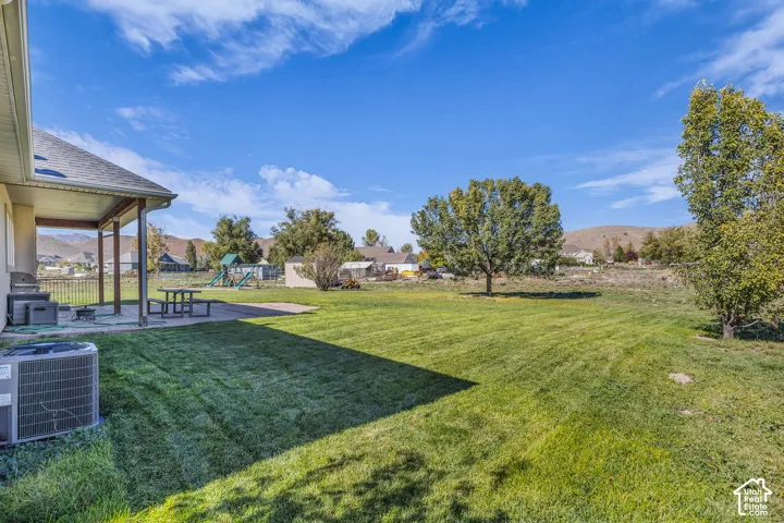 Covered concrete patio, expansive grass lawn, mature trees, and mountain backdrop