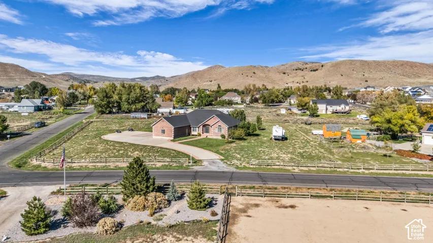 Single-story brick exterior residence featuring a curved concrete driveway, expansive lot, split-rail perimeter fencing, and mountain backdrop