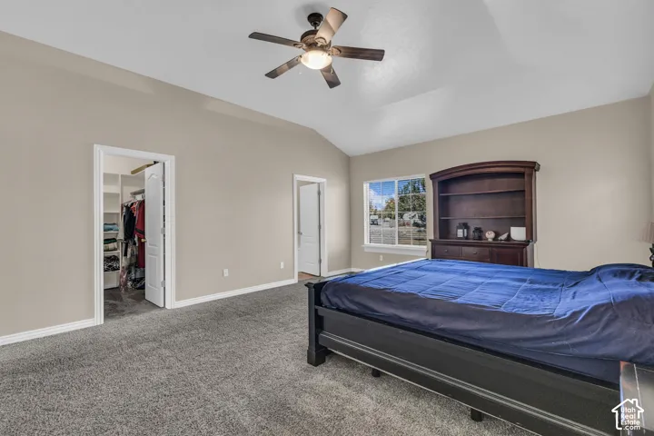 Vaulted ceilings featuring a central overhead fan and light fixture, neutral wall finishes, carpeted flooring, and a walk-in closet with built-in shelving