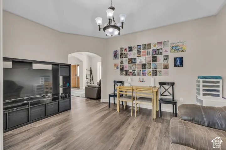 Vaulted ceiling featuring a central five-light chandelier, archway, and wood-finish flooring