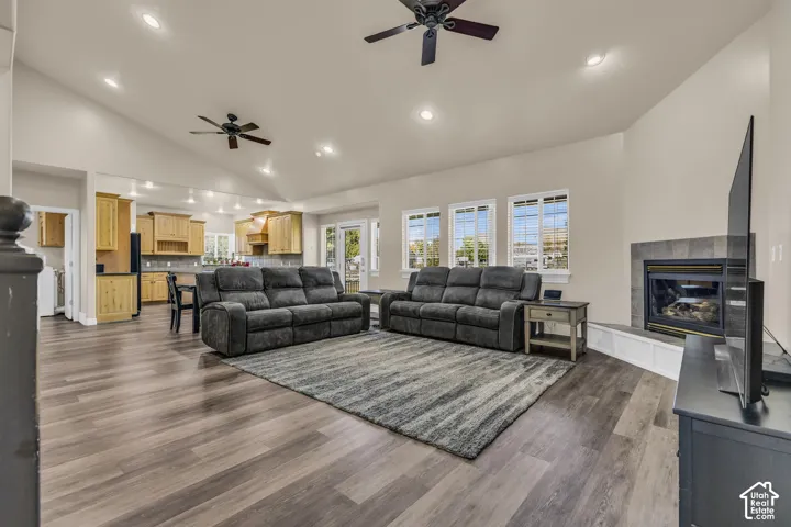 Open-concept living space featuring vaulted ceilings, wood-finish flooring, a fireplace with a stone-tile surround, multiple recessed lights, and two ceiling fans