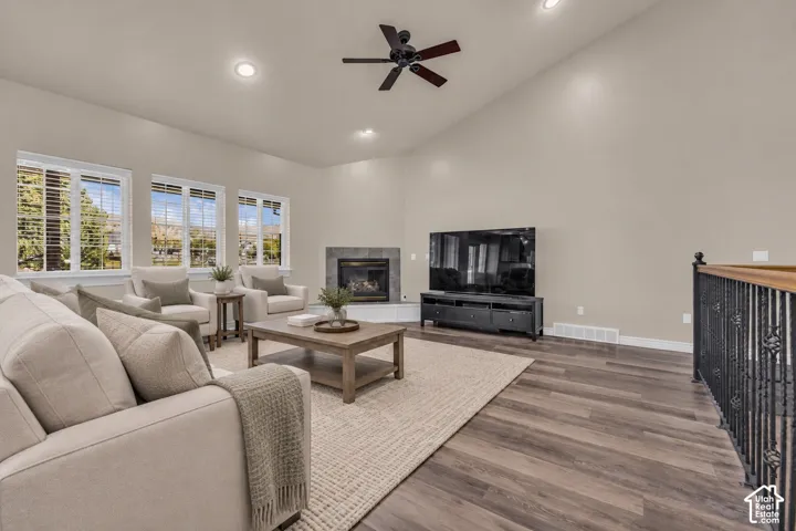 Vaulted ceilings with recessed lighting, wood-finish flooring, corner fireplace with tile surround, and wrought iron stair railing
