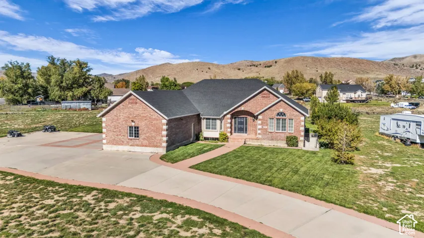 Red brick exterior with stone-accented corners, architectural shingle roof, paved driveway, and manicured lawn set against a mountain backdrop