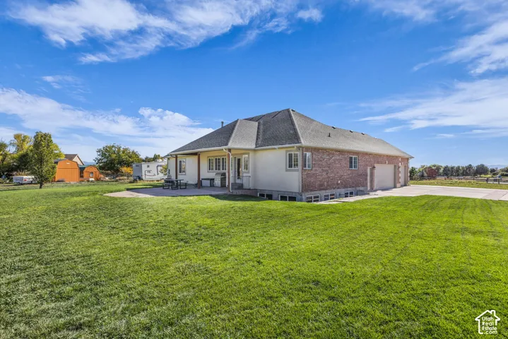 Exterior featuring a brick and stucco facade, a concrete rear patio, a multi-car garage, and a sodded lawn