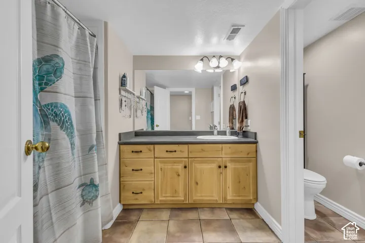 Bathroom featuring a wooden vanity, dark countertop, integrated basin, large wall-mounted mirror, and tile flooring