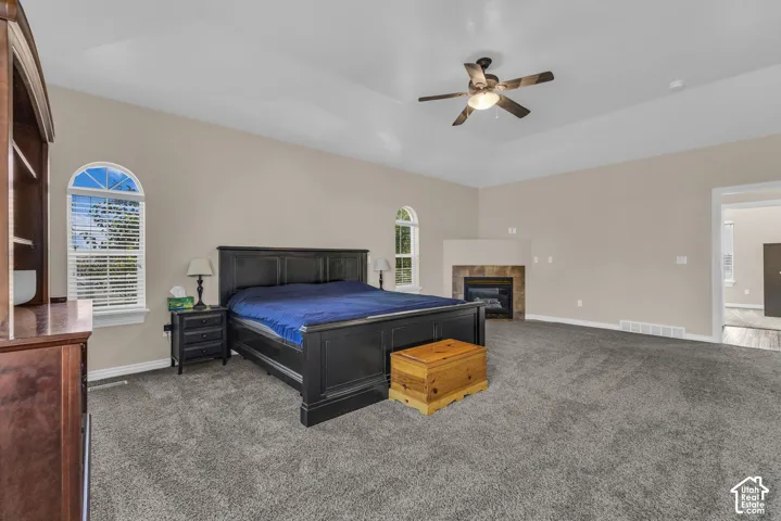 Spacious room featuring a vaulted ceiling, arched windows, a corner fireplace with stone-surround tile, and a central ceiling fan