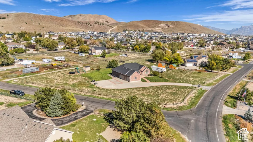 Single-story brick residence featuring a multi-car garage, expansive lot, and asphalt driveway, set against a mountainous landscape