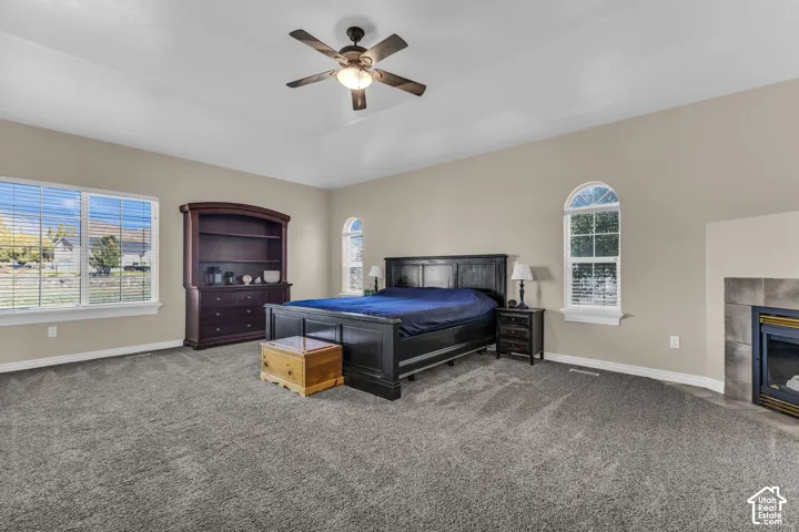 Spacious room featuring a tray ceiling, neutral wall tones, arched windows, a built-in fireplace with tile surround, and carpeted flooring