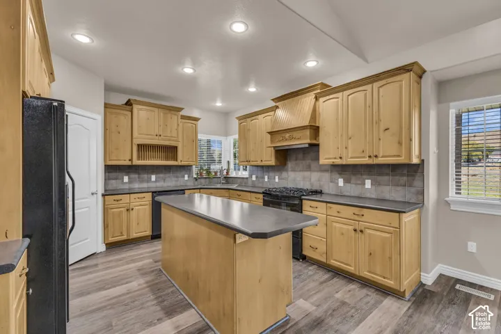 Kitchen featuring natural wood cabinetry, central island with an extended countertop, stone-tile backsplash, and wood-finish flooring