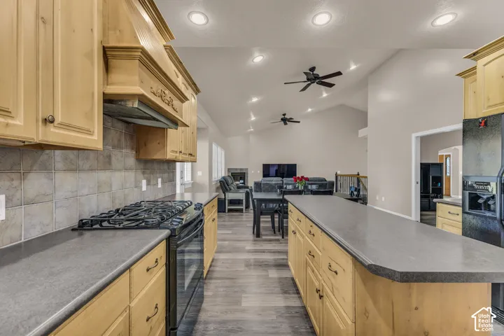 Kitchen featuring custom wood cabinetry, stone-tiled backsplash, expansive central island, wood-finish flooring, and vaulted ceilings