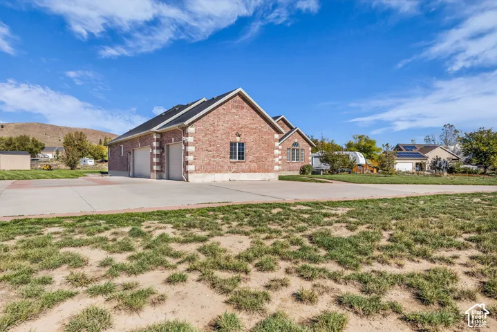 Brick exterior with stone-accented corners, multi-car garage, and expansive concrete driveway situated on a large lot