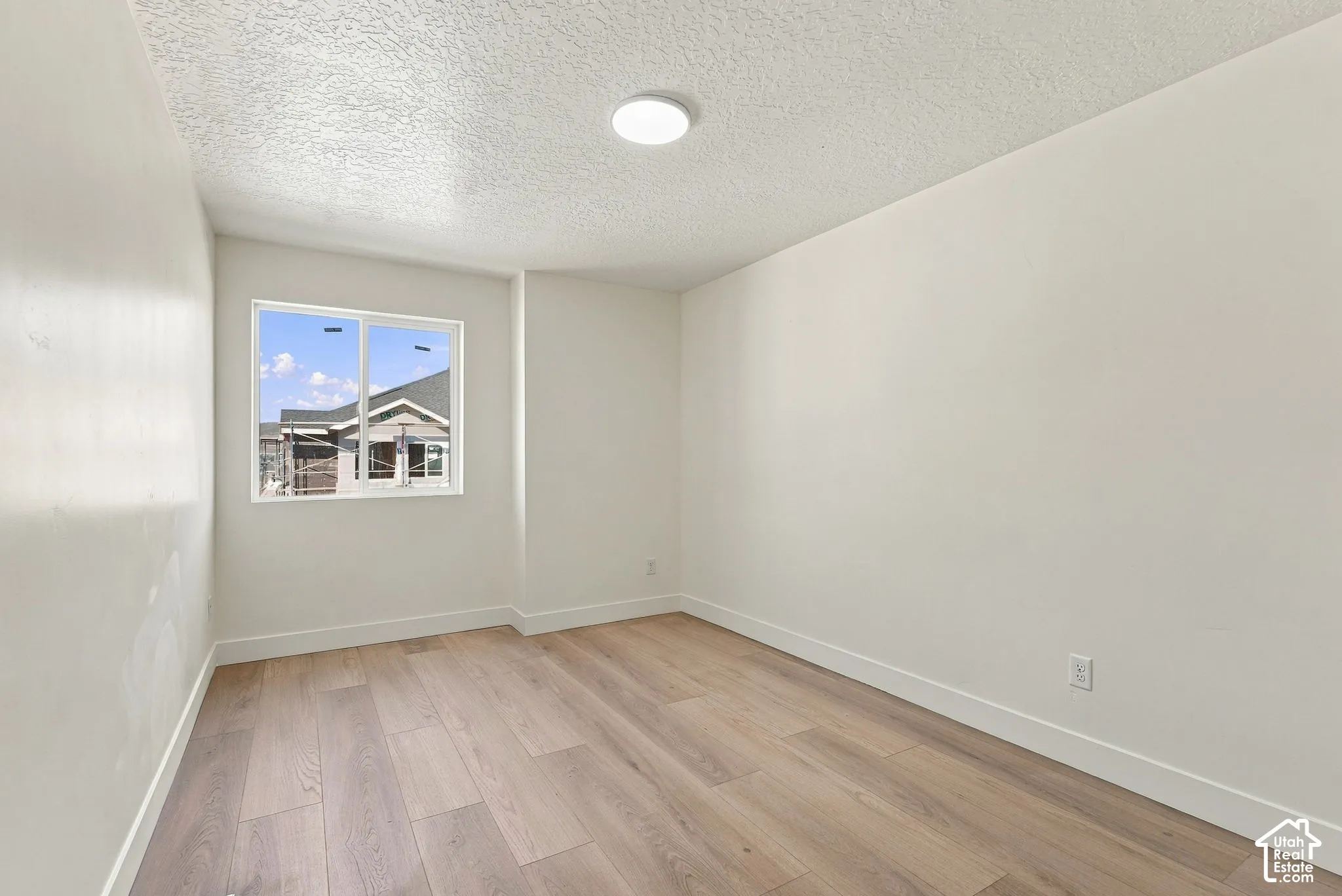 Interior room featuring wood-finish flooring, white walls, a single-pane sliding window, and a flush-mount circular ceiling light