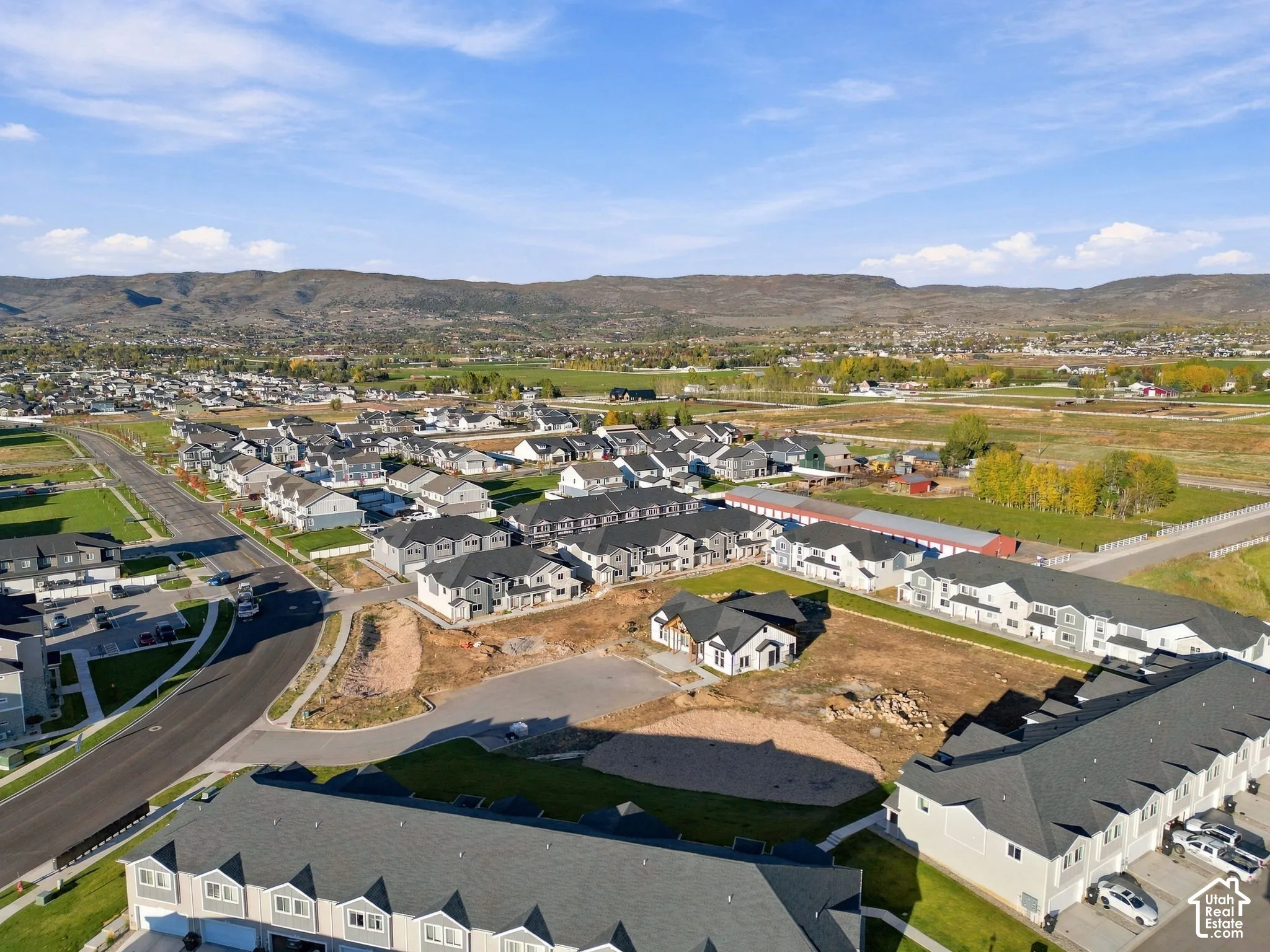 Aerial perspective of a multi-unit residential community featuring asphalt-paved streets, shingled roofing, and mountain backdrops