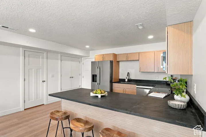 Kitchen featuring light wood-finish cabinetry, dark solid-surface countertops, recessed lighting, and stainless steel appliances