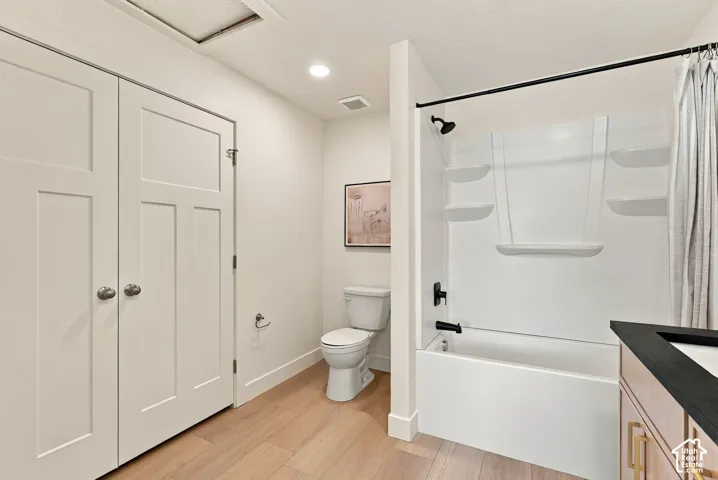 Bathroom featuring wood-finish flooring, a white vanity with a dark countertop, a bathtub-shower combination with built-in shelving, matte black fixtures, and a dual-door closet