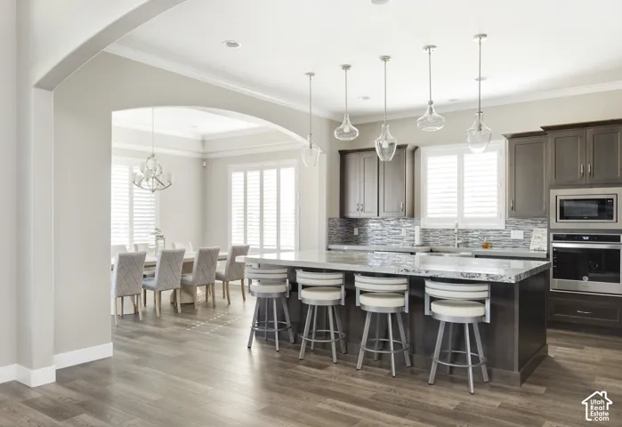 Kitchen featuring a large stone-surface island, dark wood-finish cabinetry, stacked-tile backsplash, wood-finish flooring, and pendant lighting
