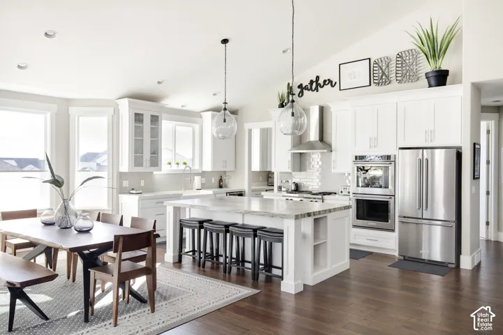 Kitchen featuring white shaker-style cabinetry, an expansive center island with countertop seating, stainless steel double wall ovens, a glass-tile backsplash, and vaulted ceilings