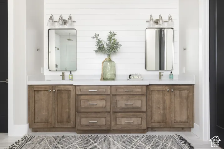 Double vanity featuring custom wood cabinetry, light-toned stone countertop, dual rectangular mirrors, and shiplap wall accent