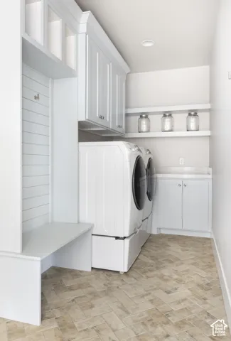 Laundry area featuring white built-in cabinetry, custom wall paneling with integrated coat hooks, a built-in bench, dual floating shelves, and herringbone tile flooring