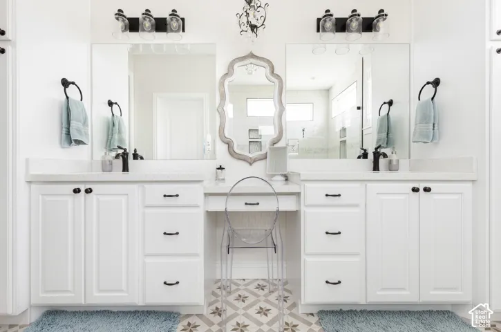 Double vanity with white cabinetry, stone-surface countertops, dual rectangular undermount sinks, patterned tile flooring, and integrated makeup station