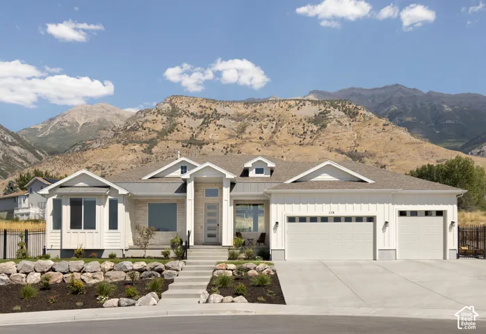 Single-story exterior featuring board-and-batten siding, stone facade accents, metal roofing details, a three-car garage, and mountain scenery