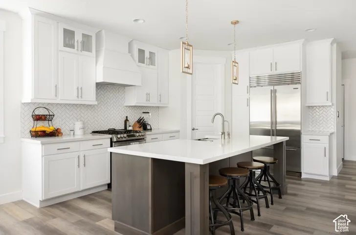 Kitchen featuring white shaker-style cabinetry, herringbone-pattern tile backsplash, quartz countertops, a central island with wood-tone base, and stainless steel built-in refrigerator