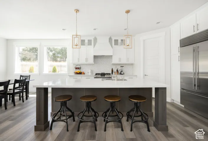 Kitchen featuring white cabinetry, quartz countertops, a herringbone-patterned tile backsplash, wood-finish flooring, and a large center island with a dark-tone base