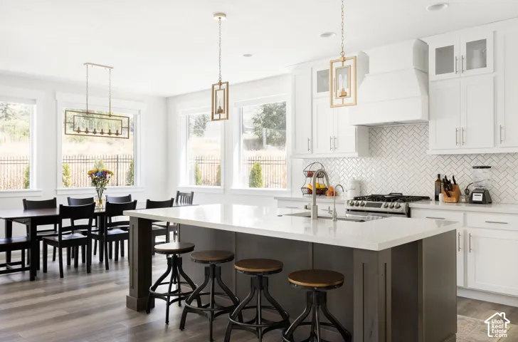 Kitchen featuring a large island with a stone countertop, white shaker-style cabinetry, a herringbone-patterned tile backsplash, and decorative pendant lighting