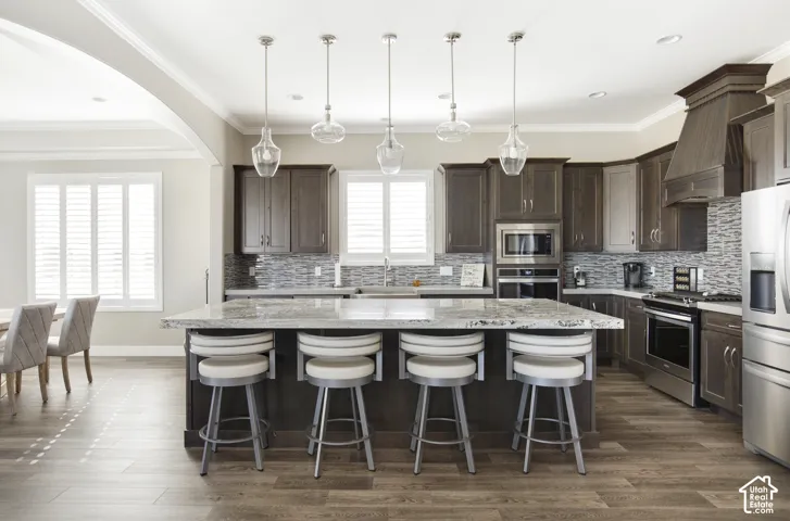 Kitchen featuring dark-finish cabinetry, a stone-surface island, mosaic tile backsplash, stainless steel appliances, and glass pendant lighting