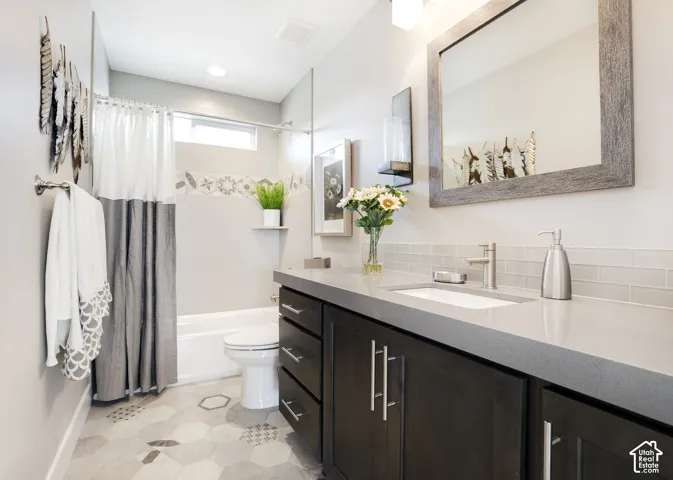 Bathroom featuring a vanity with dark-finish cabinetry, a rectangular undermount sink, and a stone-composite countertop paired with a subway tile backsplash