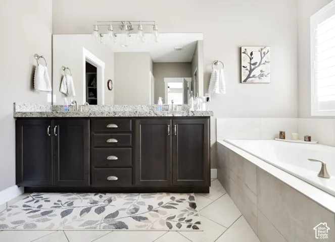 Dark wood cabinetry with brushed nickel hardware, dual-sink vanity with stone-surfaced countertop, large wall-mounted mirror, and tile-surround soaking tub