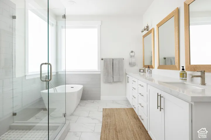 Freestanding soaking tub, walk-in glass-enclosed shower, dual-sink vanity with stone-surface countertop, white cabinetry, and tile flooring
