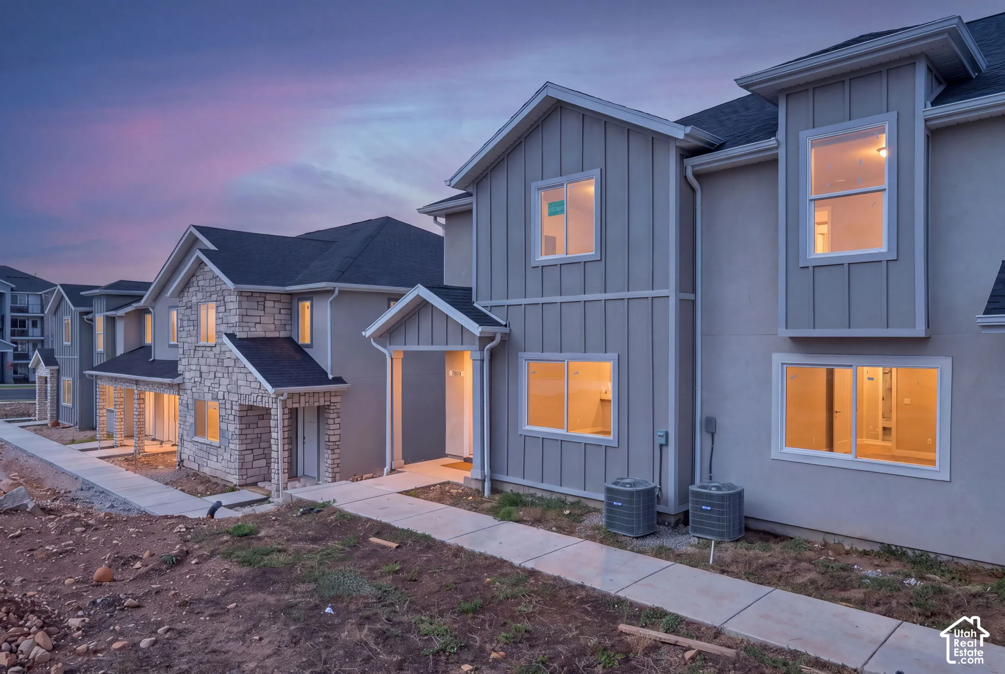 Multi-family exterior featuring board-and-batten siding, stone veneer accents, pitched rooflines, and concrete walkways