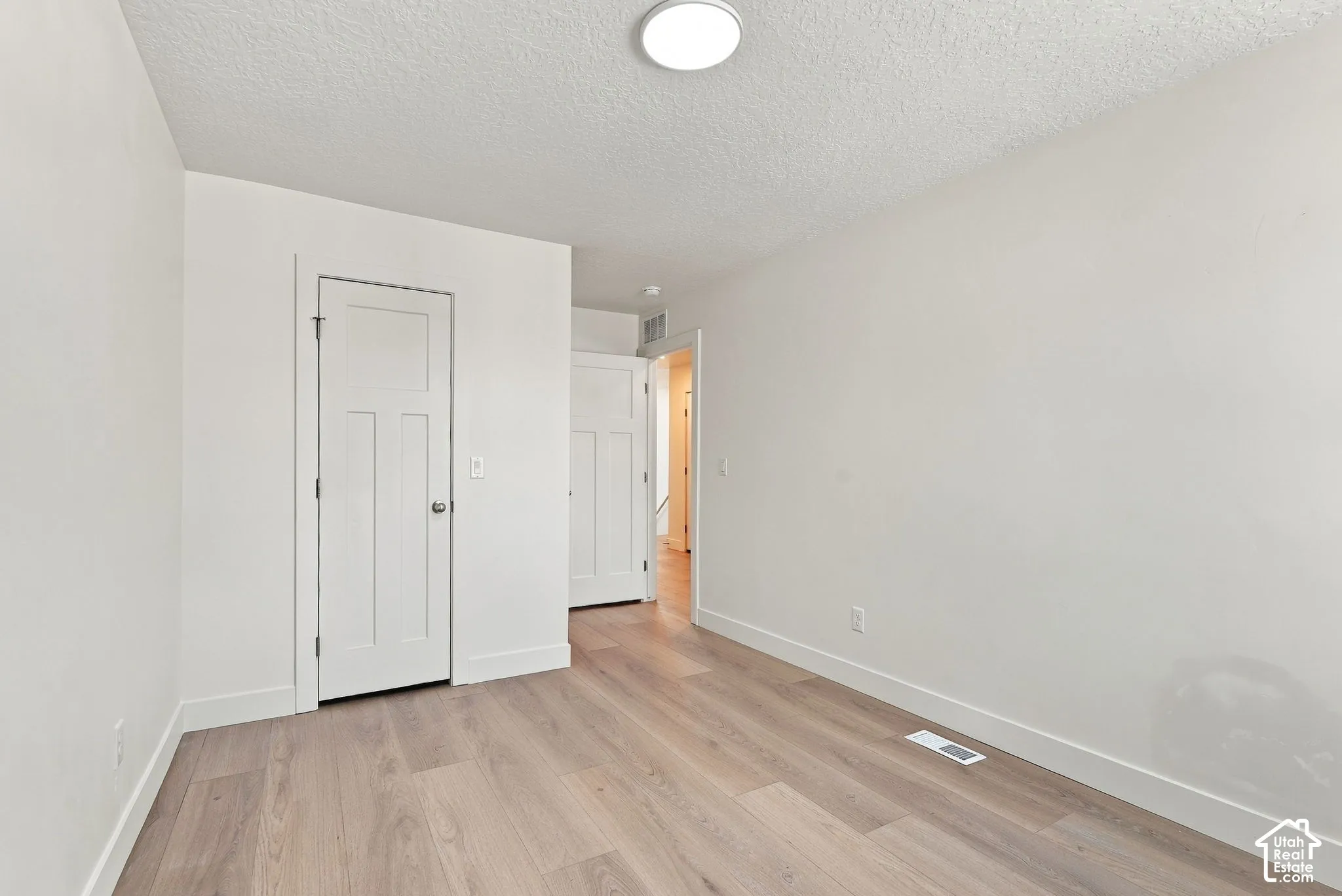 Interior room featuring wood-finish flooring, white walls, and two-panel shaker-style interior doors with brushed nickel hardware
