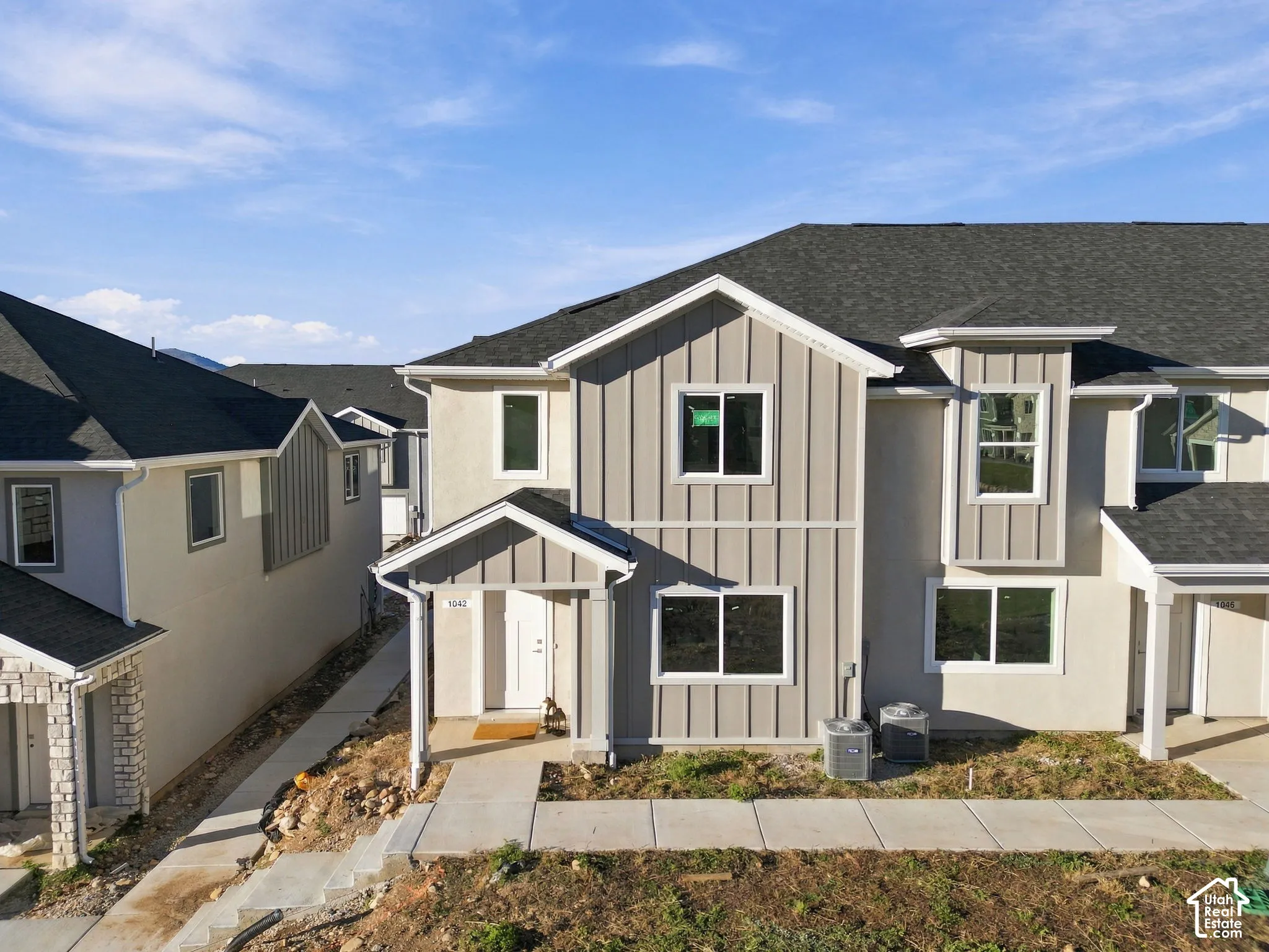 Multi-family exterior featuring board-and-batten siding, asphalt shingle roofing, concrete walkways, and covered entryway