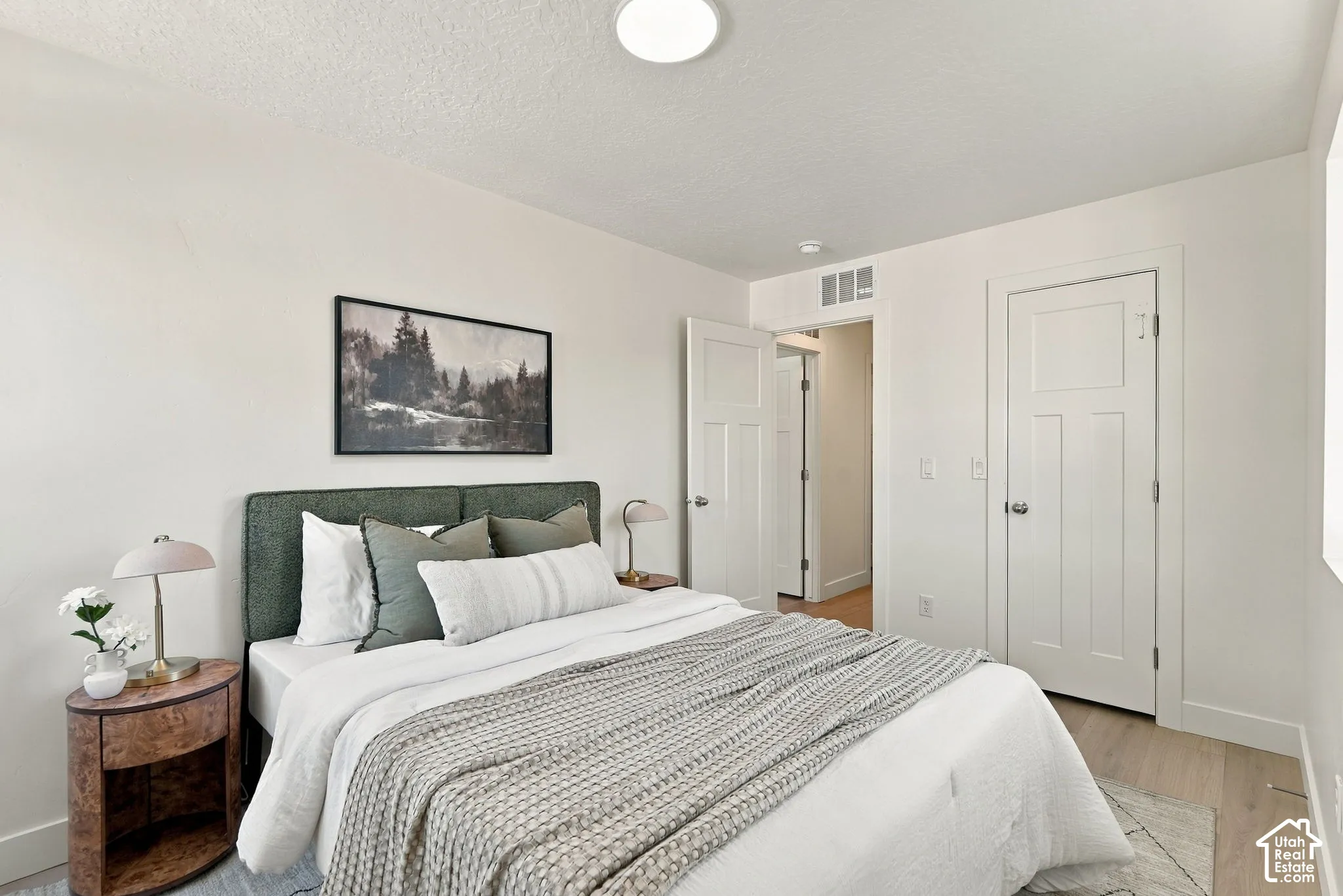 Neutral interior space featuring wood-finish flooring, crisp white walls, and a shaker-style panel door